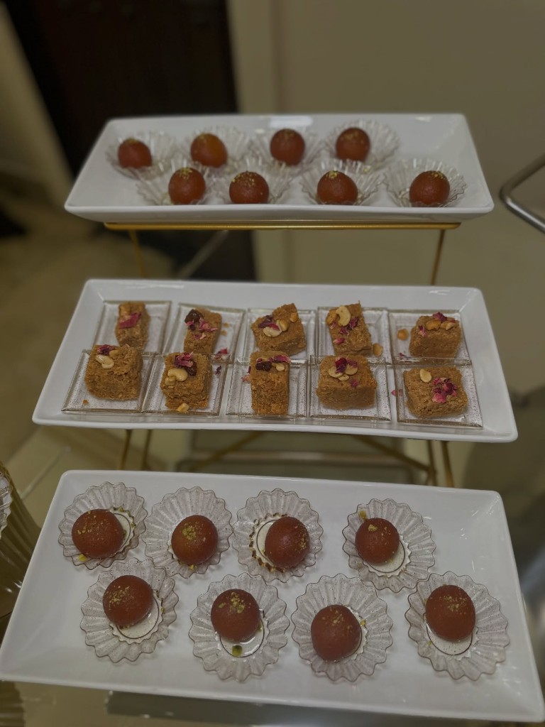 Gulab jamun and mohanthal barfi arranged on a tiered dessert display